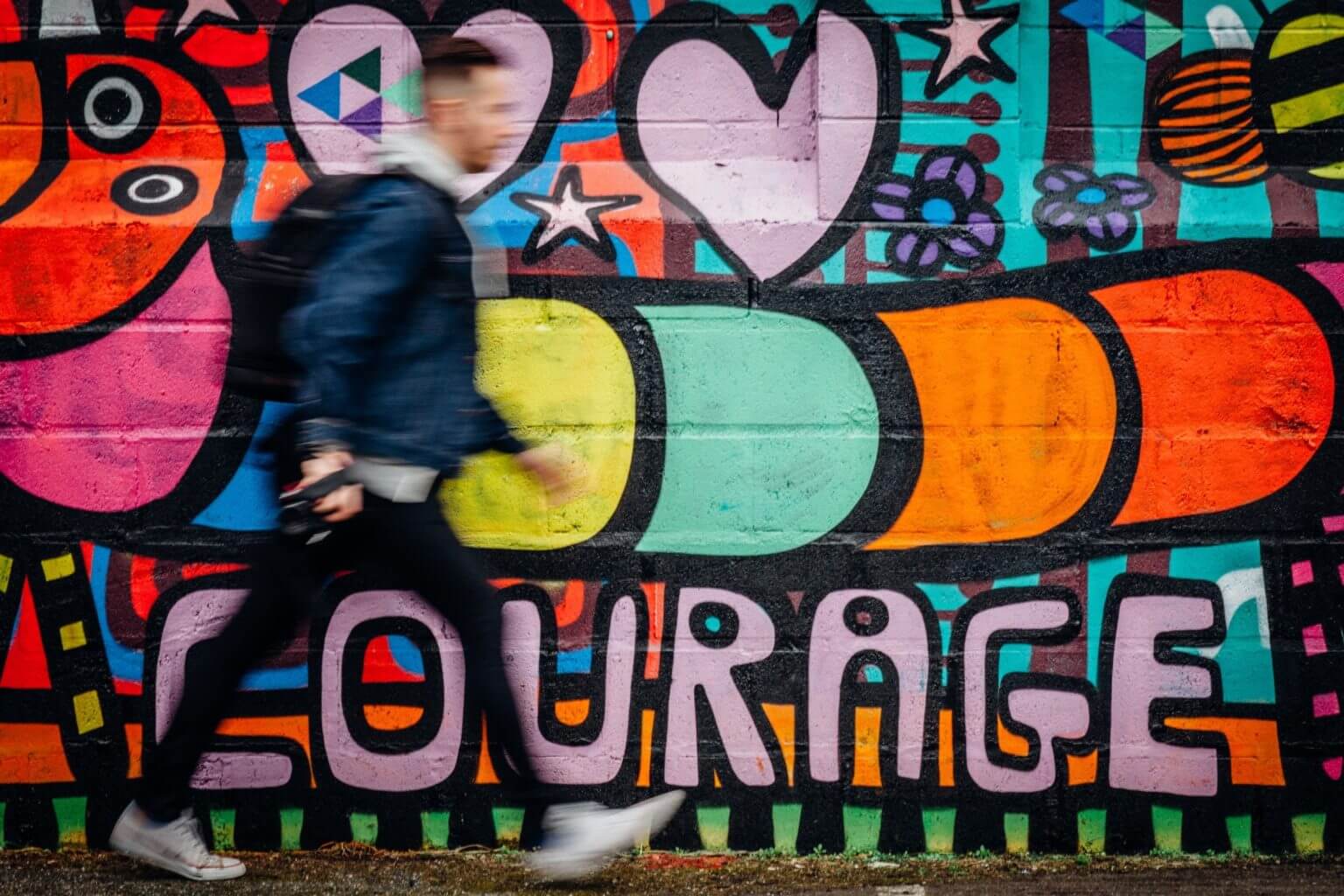 Man walking in front of graffiti that says courage